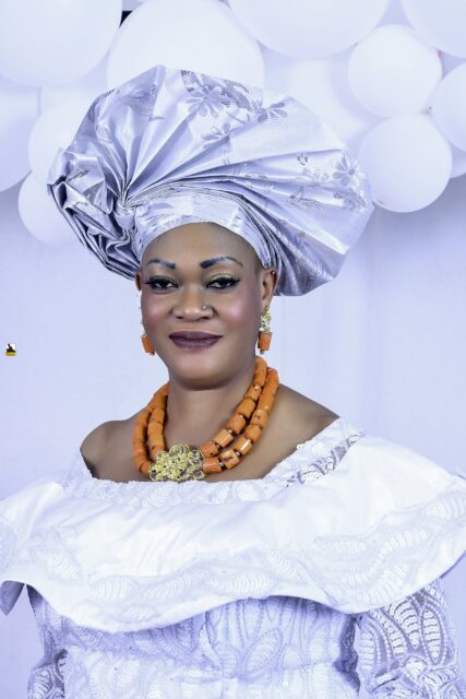 Woman in a white blouse, blue wrapper and silver headwrap by the balloons
