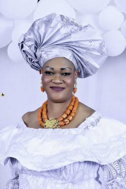 Woman in a white blouse, blue wrapper and silver headwrap by the balloons