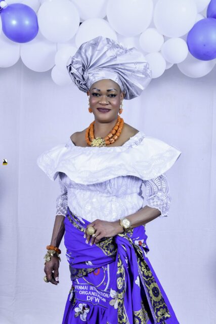 Woman in a white blouse, blue wrapper and silver headwrap by the balloons