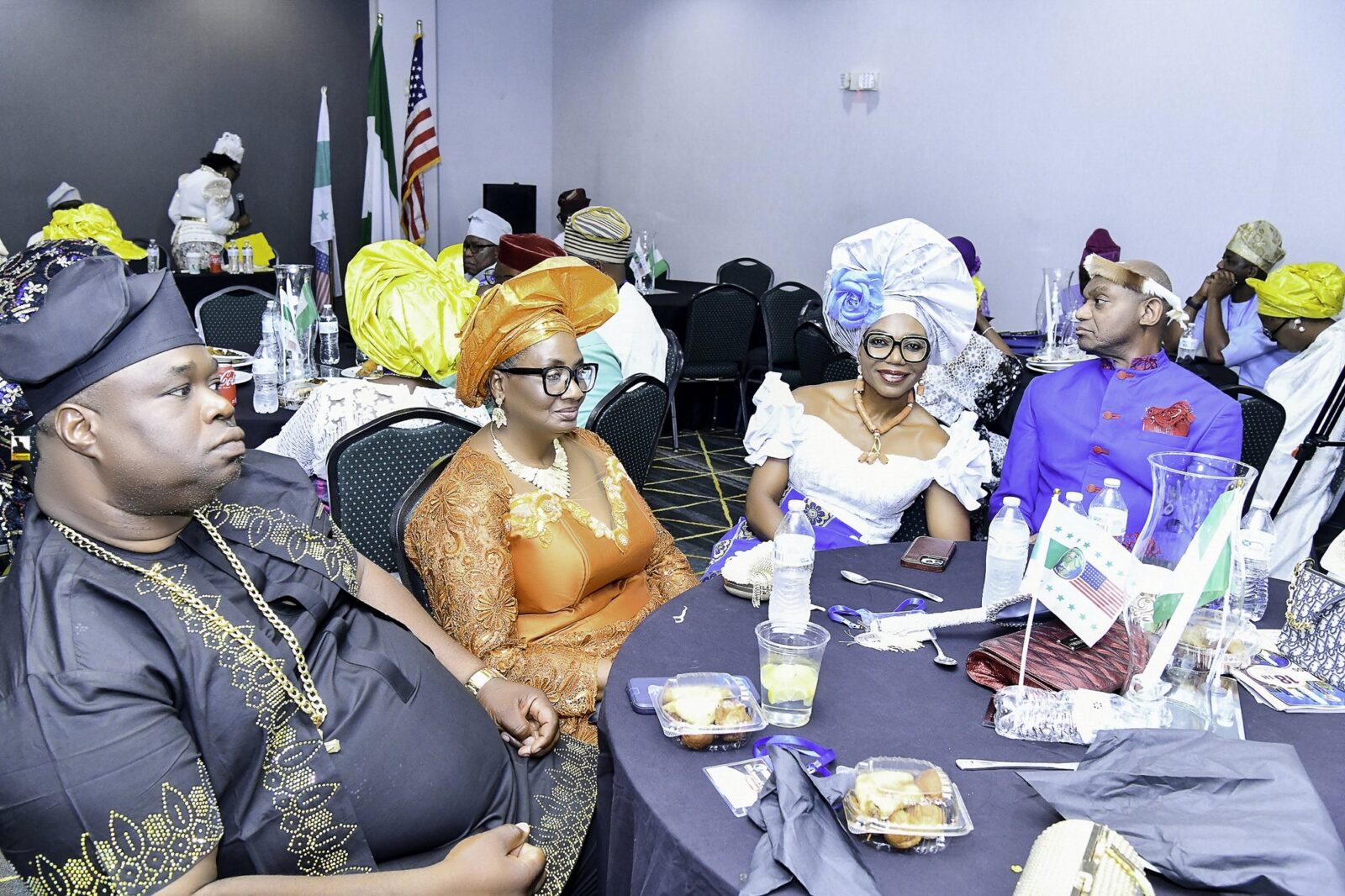 Attendees in colorful headwraps seated around a table with small flags