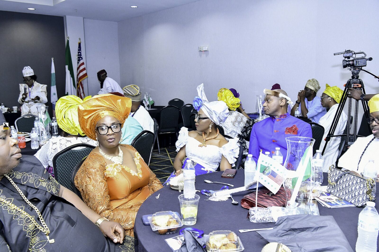 Attendees in colorful headwraps seated around a table with small flags