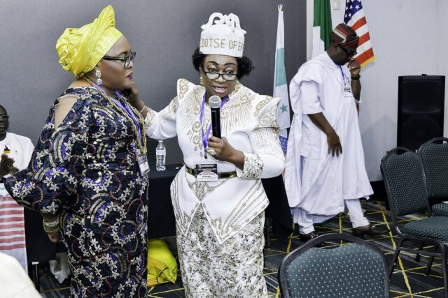 Two women standing together, one holding a microphone beside the flags