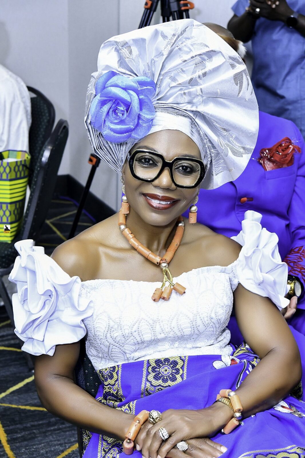 Smiling woman in a silver headwrap and glasses seated in the room