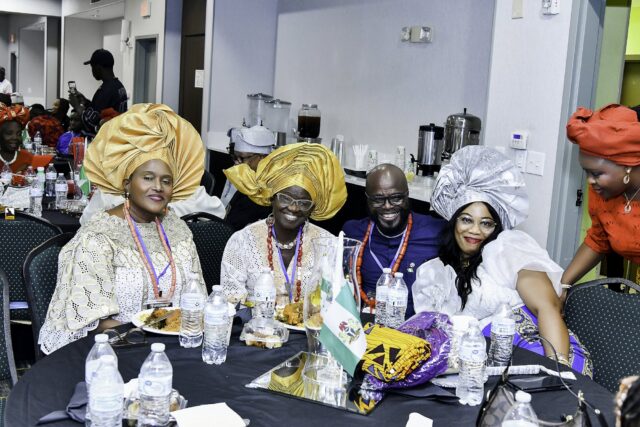 Attendees gathered around a table, including two women in gold headwraps