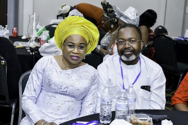 Woman in a yellow headwrap seated beside a man in white clothing