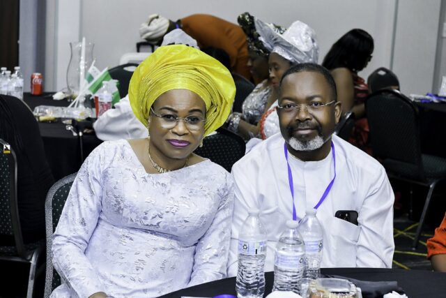 Woman in a yellow headwrap seated beside a man in white clothing