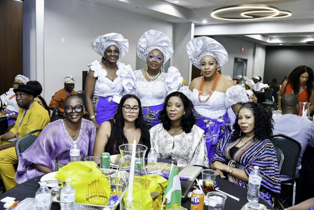 Women in white, blue and patterned clothing gathered around a table