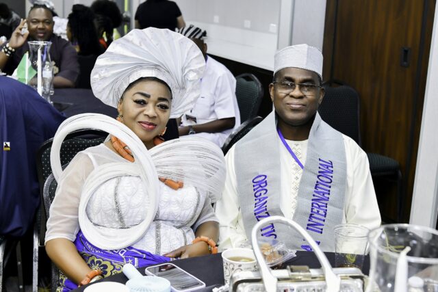 Woman in a silver headwrap and man in a dark cap seated together