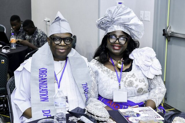 Two smiling attendees in pale clothing and headwear seated together