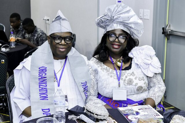 Two smiling attendees in pale clothing and headwear seated together