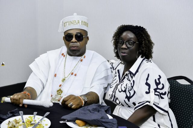 Man in white with sunglasses and woman in a patterned top at a table