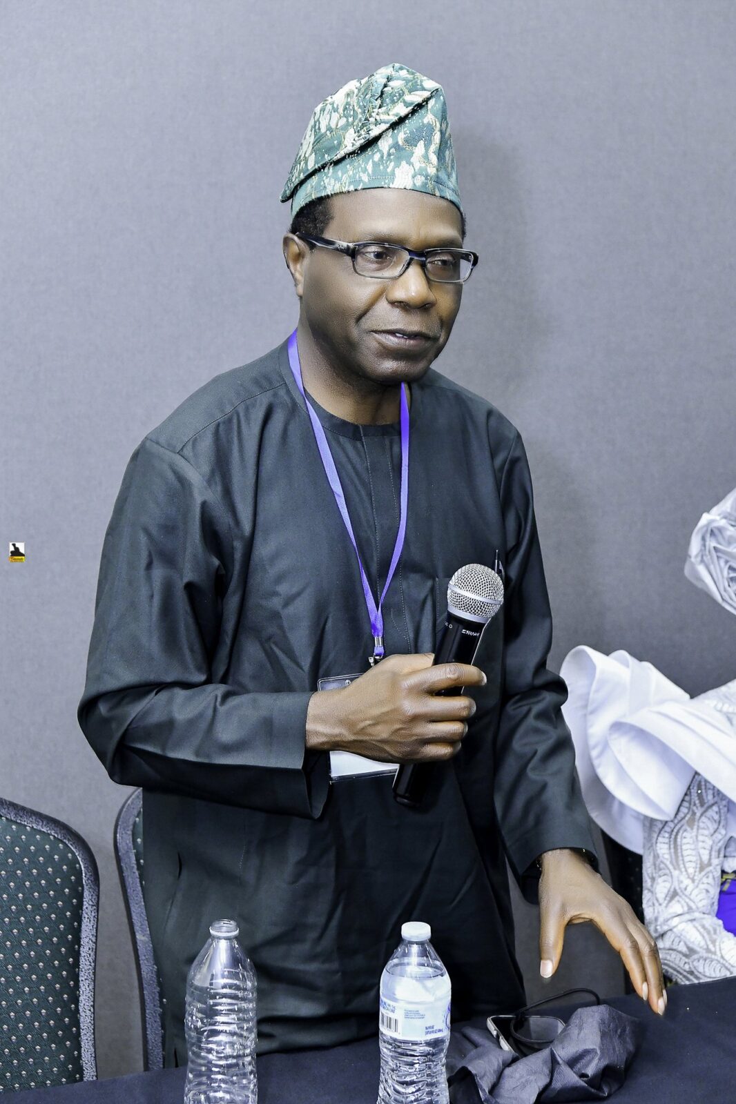 Man in dark clothing and a green cap holding a microphone
