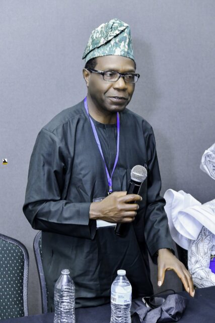 Man in dark clothing and a green cap holding a microphone