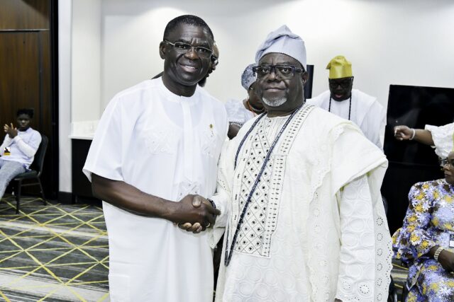Two smiling men in white clothing shaking hands in the convention room