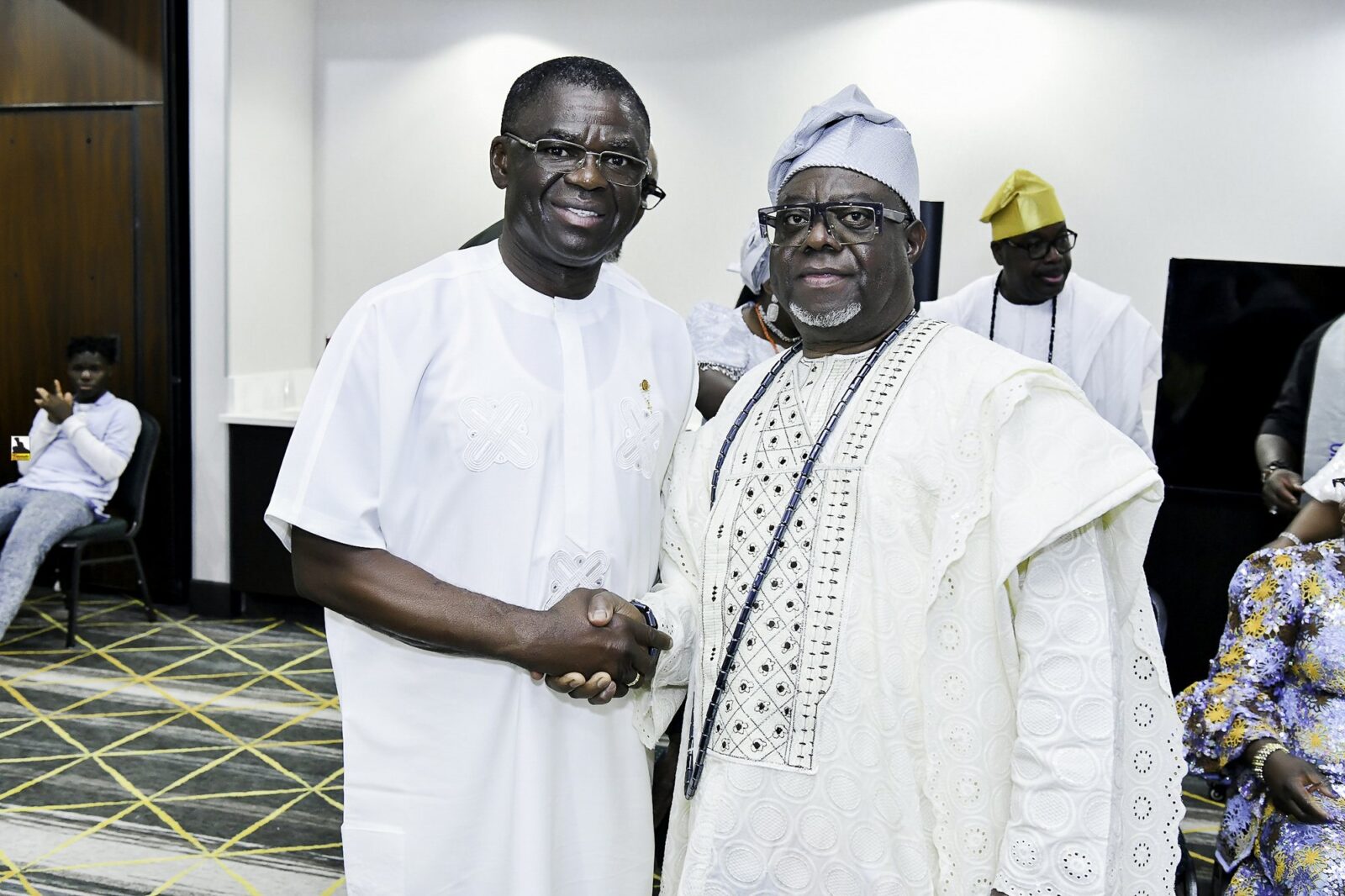 Two smiling men in white clothing shaking hands in the convention room