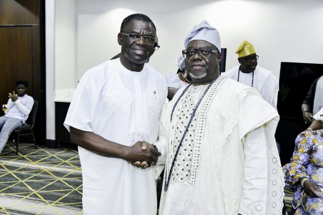 Two smiling men in white clothing shaking hands in the convention room
