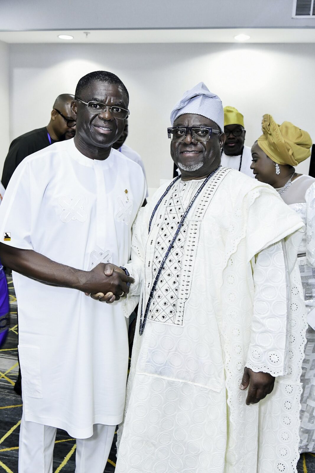 Two smiling men in white clothing shaking hands in the convention room
