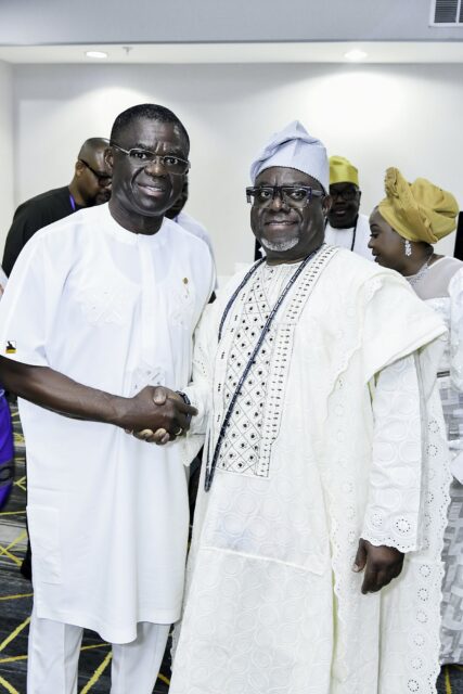 Two smiling men in white clothing shaking hands in the convention room