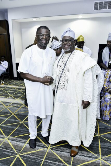Two smiling men in white clothing shaking hands in the convention room