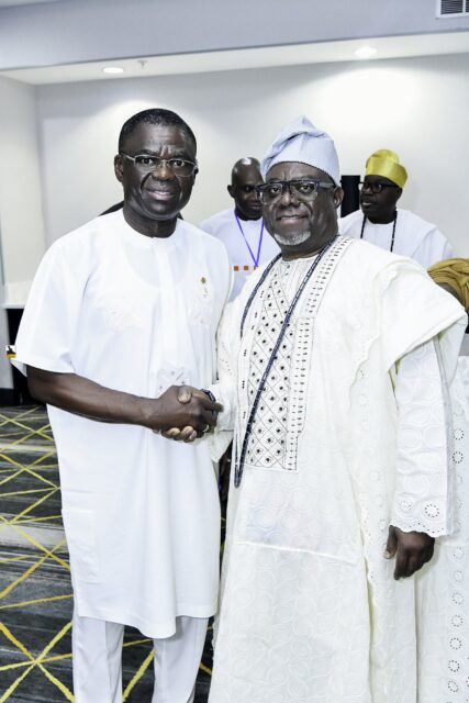Two smiling men in white clothing shaking hands in the convention room