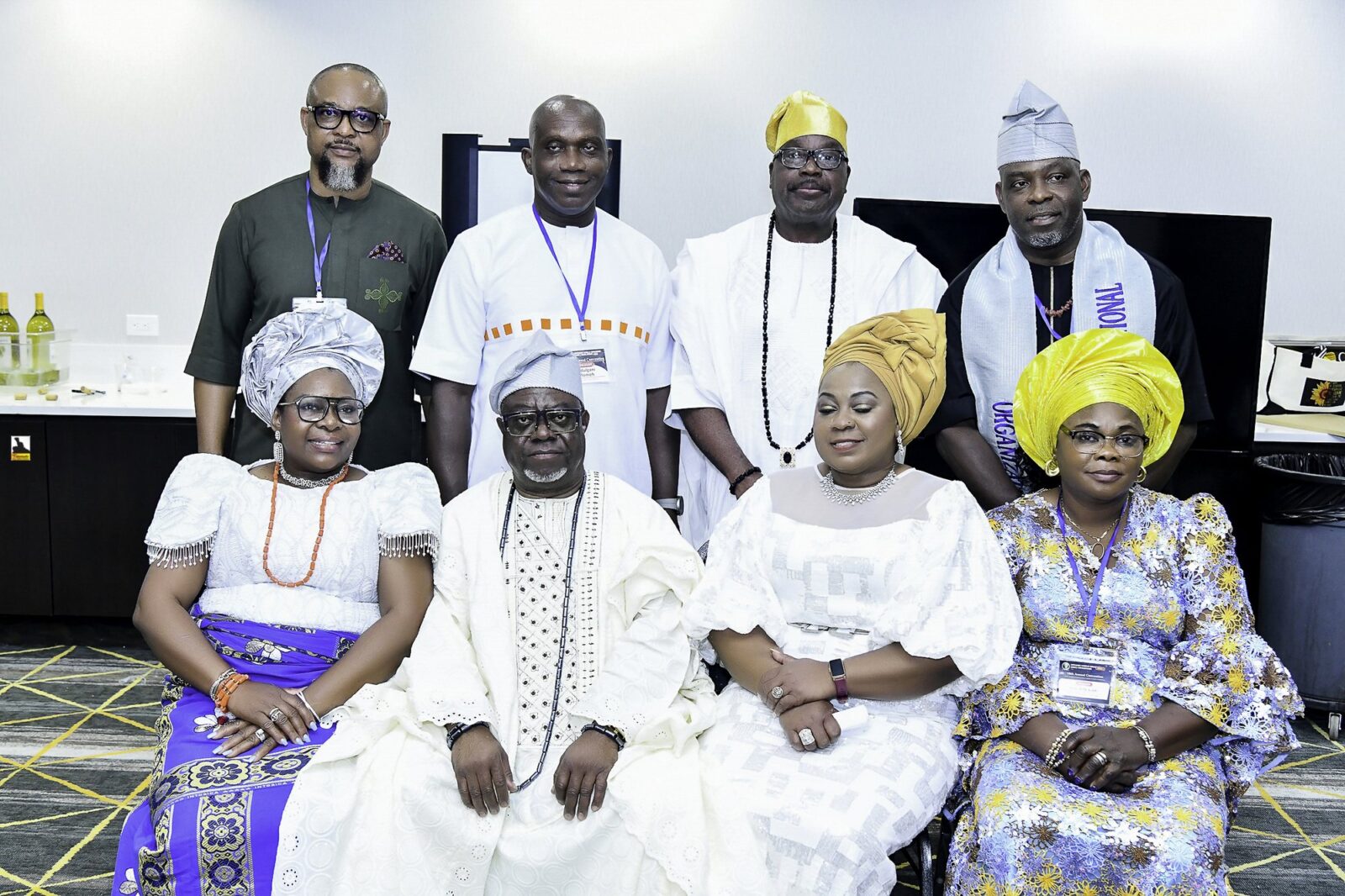 Eight attendees in white, blue and green clothing posing in two rows