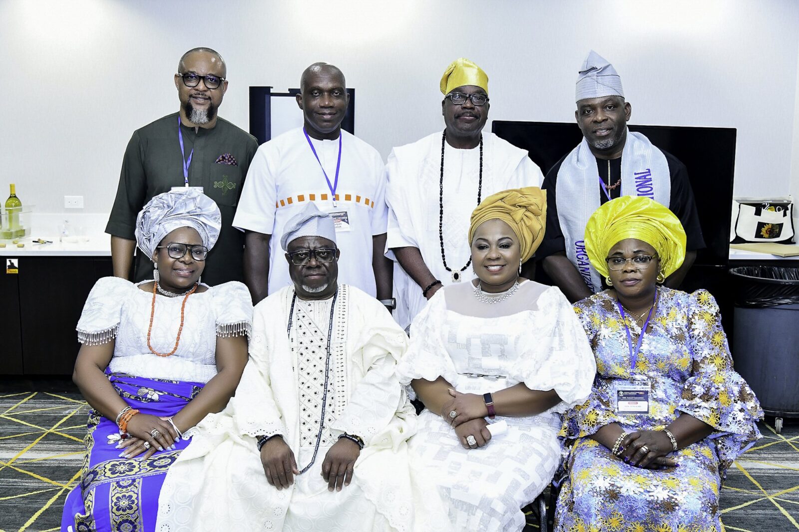 Eight attendees in white, blue and green clothing posing in two rows