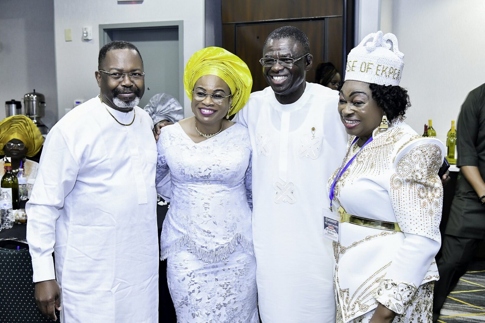 Four smiling attendees standing together in white clothing and bright headwear