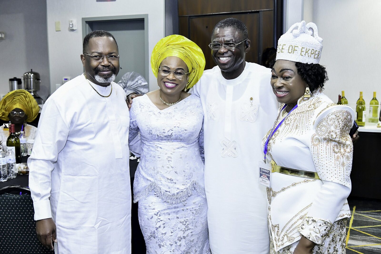 Four smiling attendees standing together in white clothing and bright headwear